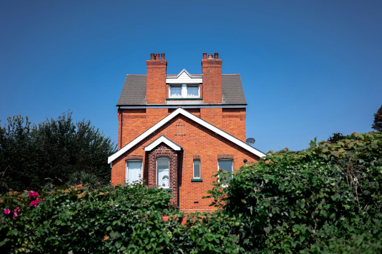 Red brick house surrounded by green bushes.